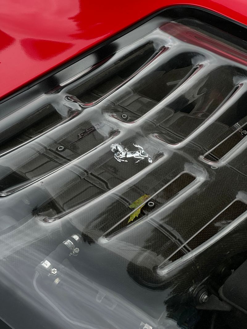 Close-up of a red Ferrari’s louvred clear engine cover, with the prancing horse visible on the engine beneath.