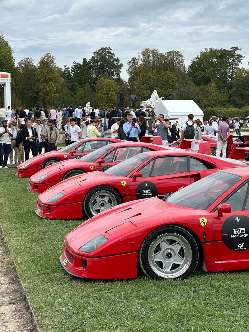 Four red Ferrari F40s parked nose to tail on the grass, with a crowd behind them.
