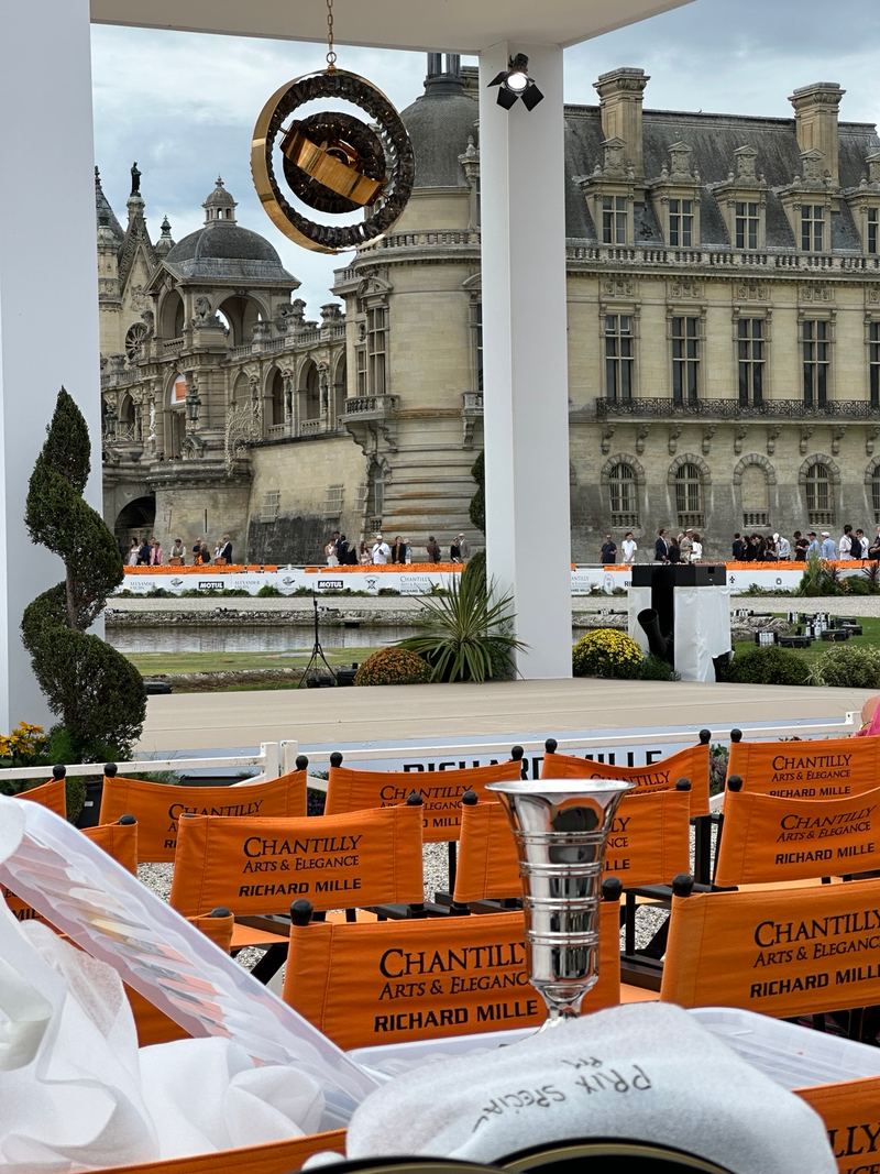 The prize-giving stage in front of the château, with orange event chairs and a silver trophy in the foreground.