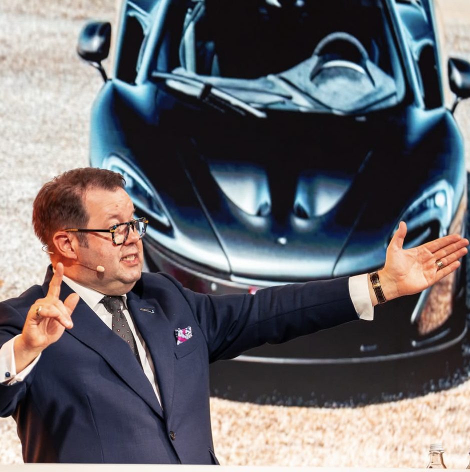 El subastador gesticulando delante de un McLaren P1 en pantalla