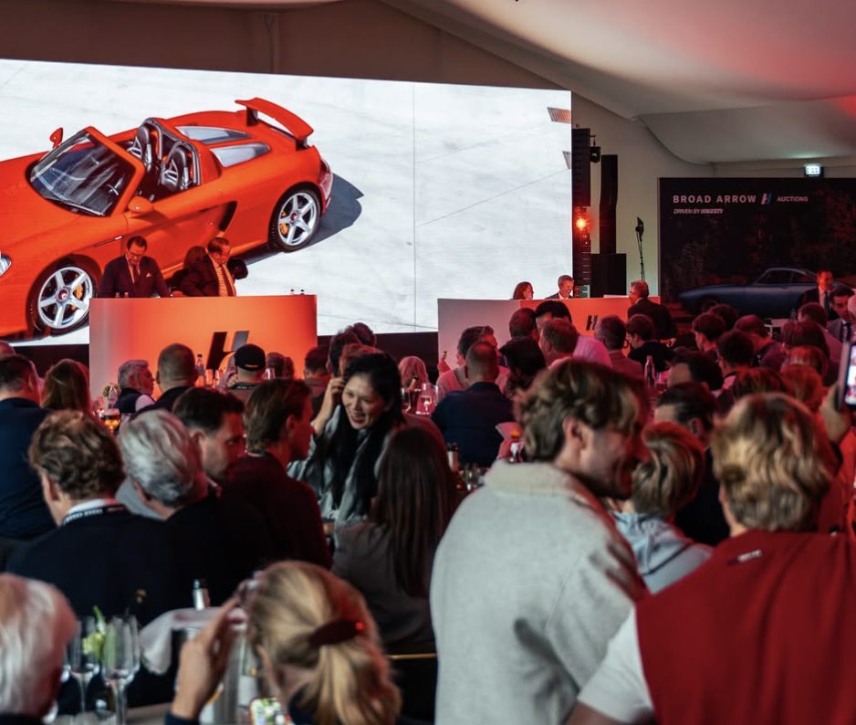 Una sala de subastas llena mirando un Porsche Carrera GT en una gran pantalla